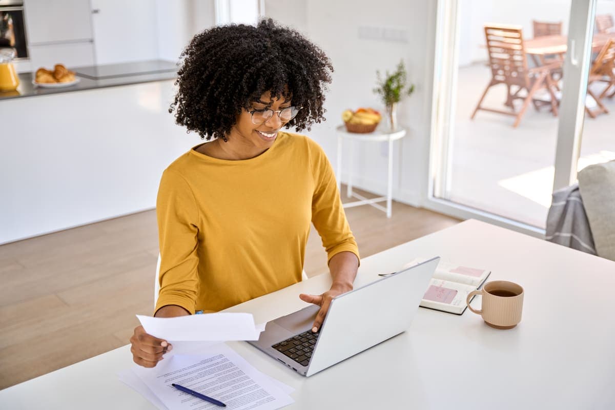 A first-time buyer reviewing mortgage paperwork with a laptop at a kitchen table.