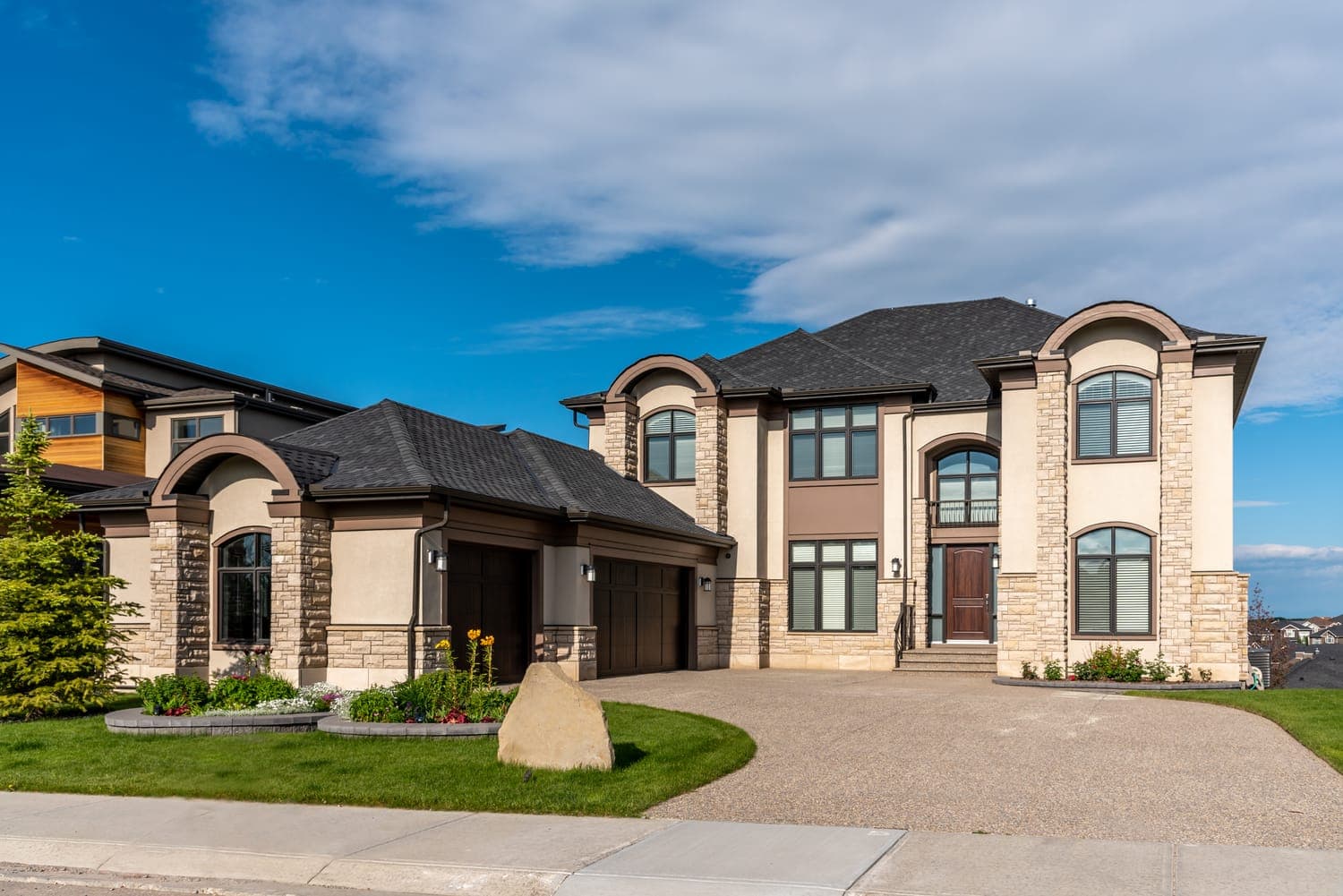 An elegant suburban home with manicured landscaping under a bright blue sky.